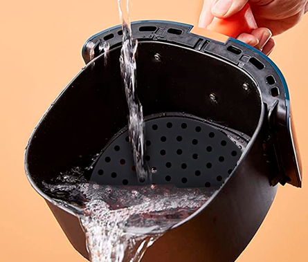 Una cesta de freidora de aire que se lava con agua. La cesta es negra con una base perforada.