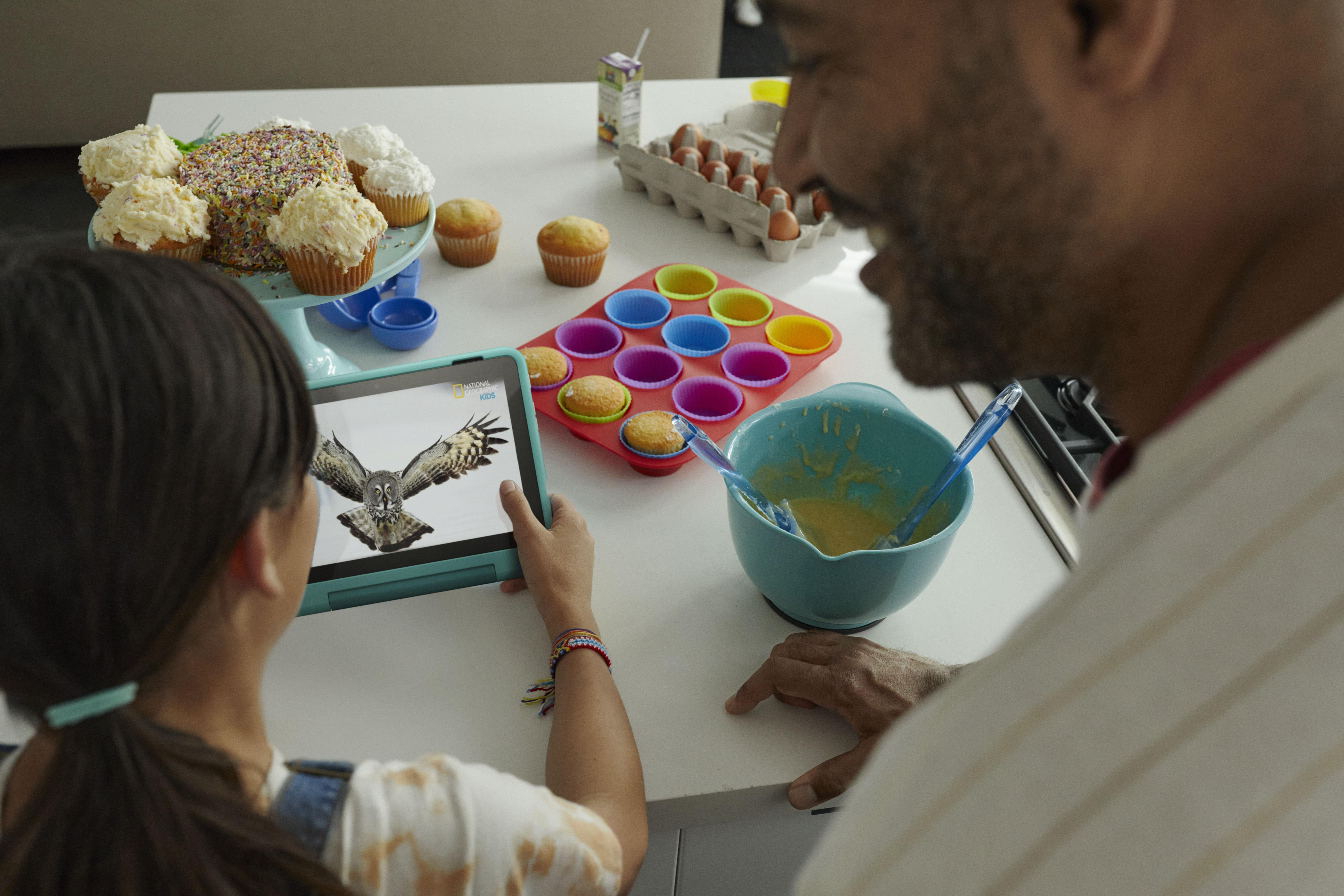 Ein Mädchen und ein Mann betrachten ein Tablet. Auf dem Tisch stehen Cupcakes, Eier und Teig.