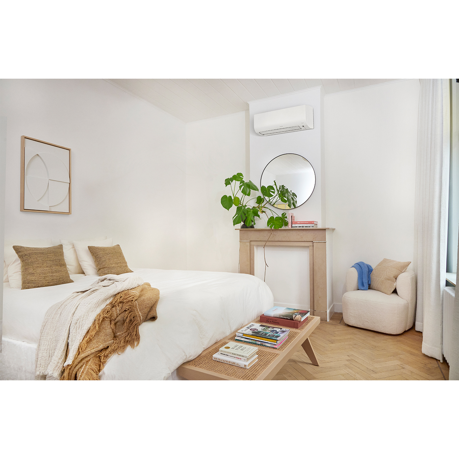 Camera da letto con letto, panca con libri, specchio, dipinto e pianta.