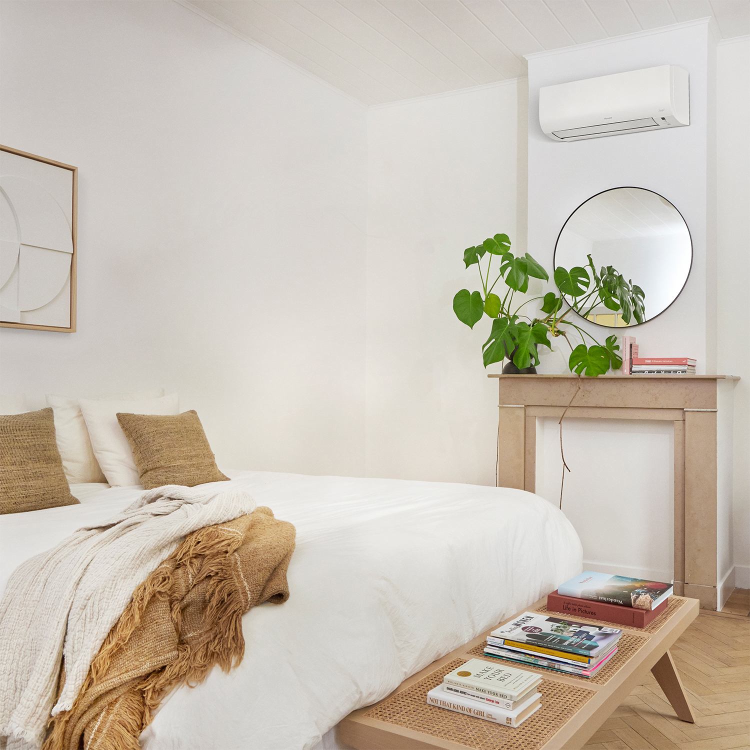 Una camera da letto con un letto bianco, una panca e un grande specchio. Una pianta è sul camino.