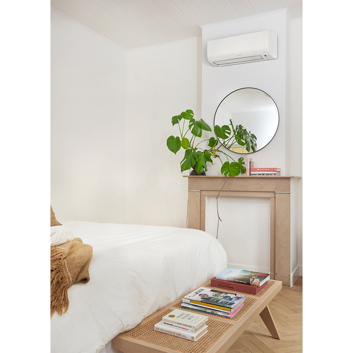 Camera da letto con letto, panca, specchio e pianta. Muri bianchi e pavimento in legno chiaro.
