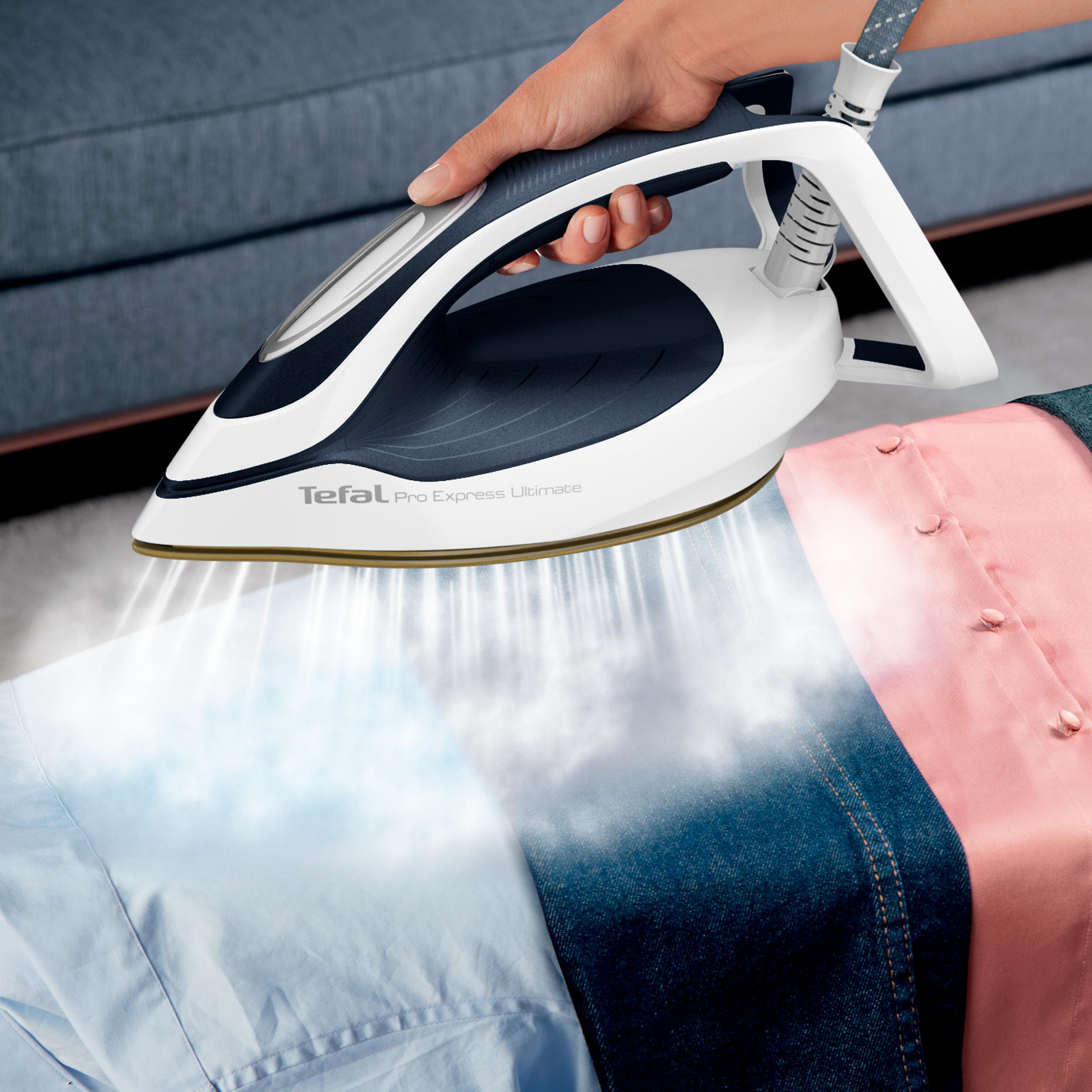 Eine Person bügelt Hemden mit einem Tefal-Bügeleisen und erzeugt Dampf über blauen und rosa Hemden. Das Bügeleisen ist weiß und blau.