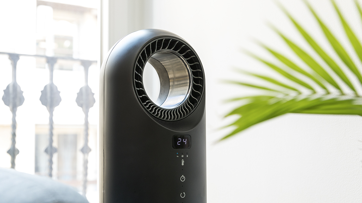 Purificador de aire negro con pantalla digital que muestra 24. Una planta verde y una ventana con barandilla decorativa al fondo.