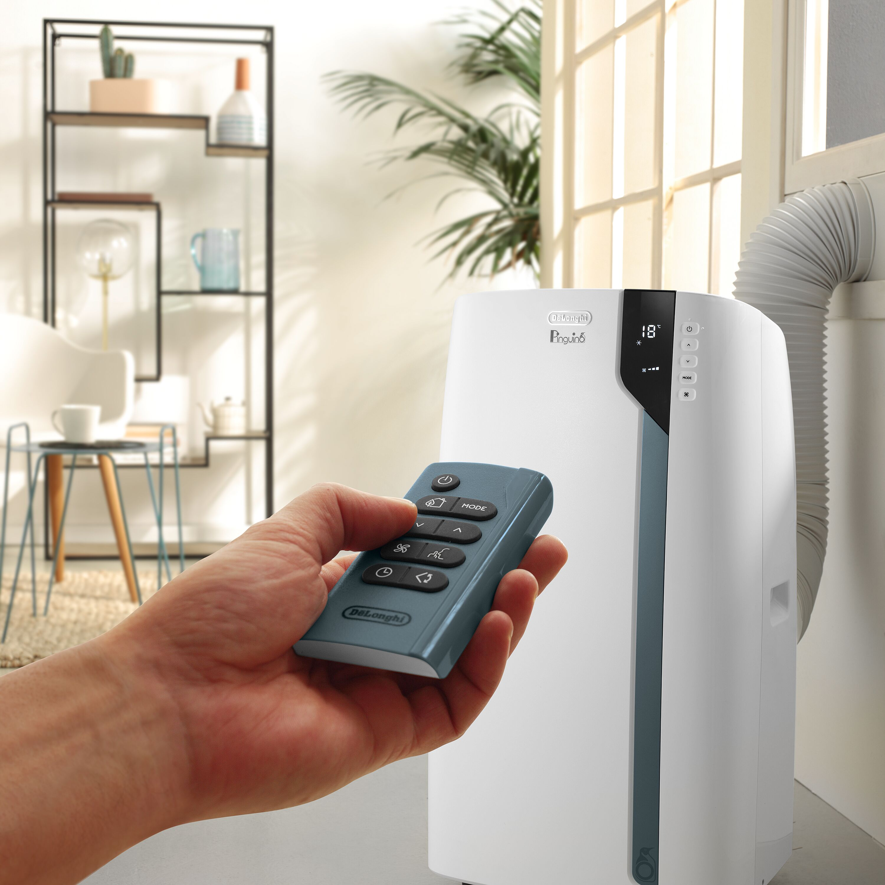 Hand hält Fernbedienung in der Nähe eines weißen Klimageräts.