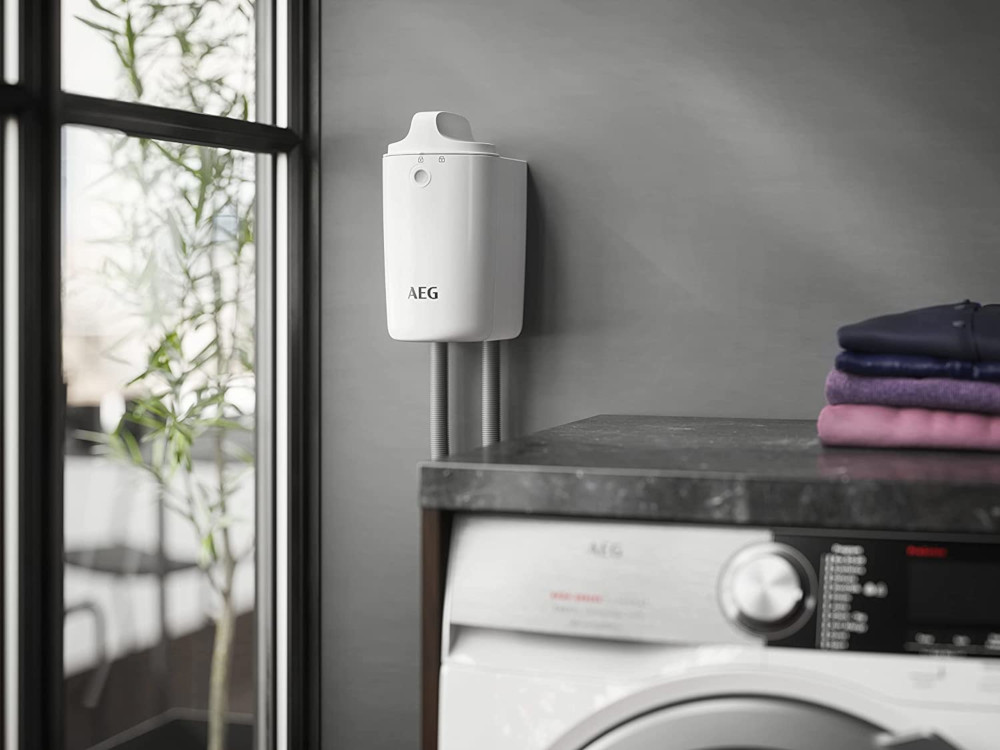 Wit wandapparaat boven een wasmachine en een wasmand, binnenomgeving.