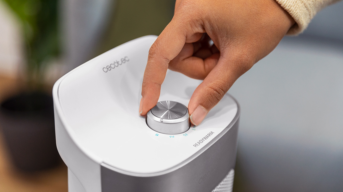 Una mano gira una perilla plateada en un dispositivo blanco y plateado con la etiqueta 'READYWARM'.