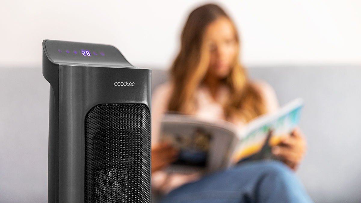 Un calefactor negro muestra 28 grados. Una mujer lee una revista borrosa en el fondo. El calefactor está enfocado.