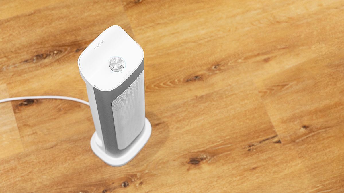 Un calefactor eléctrico blanco y gris sobre piso de madera. El calefactor está a la izquierda, con un dial arriba. Sale un cable.