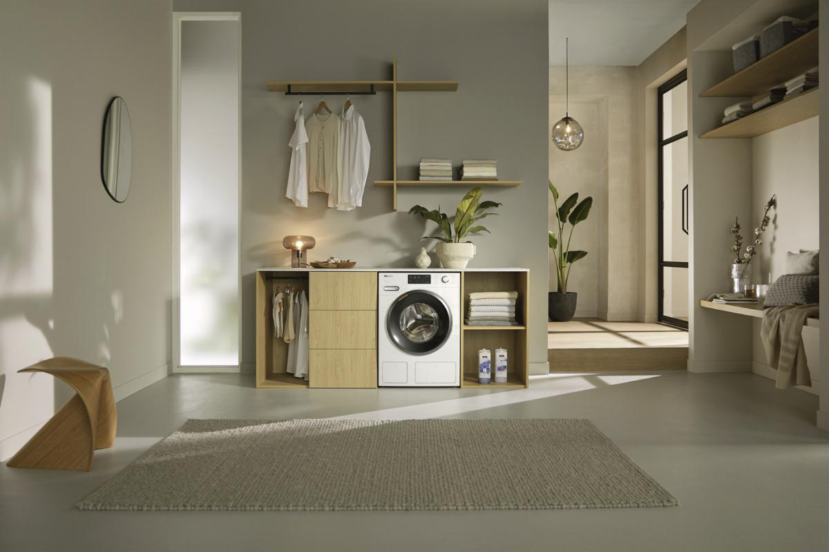 Ein Waschraum mit Waschmaschine, Holzschränken, Kleidung, Teppich und Pflanzen. Der Raum ist hell und modern.