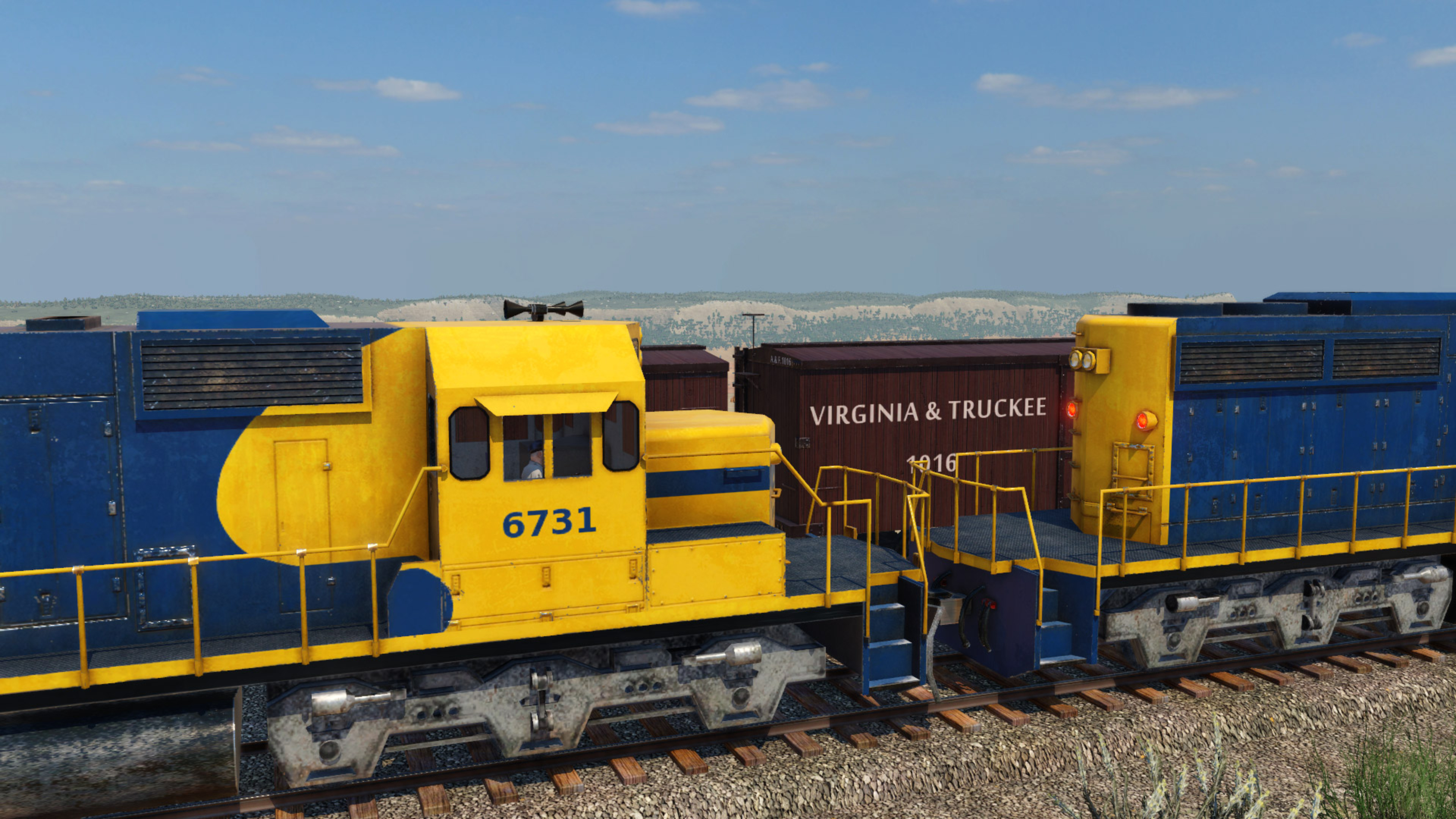 Eine gelb-blaue Lok auf Gleisen. Im Hintergrund braune Waggons und ein blauer Himmel.