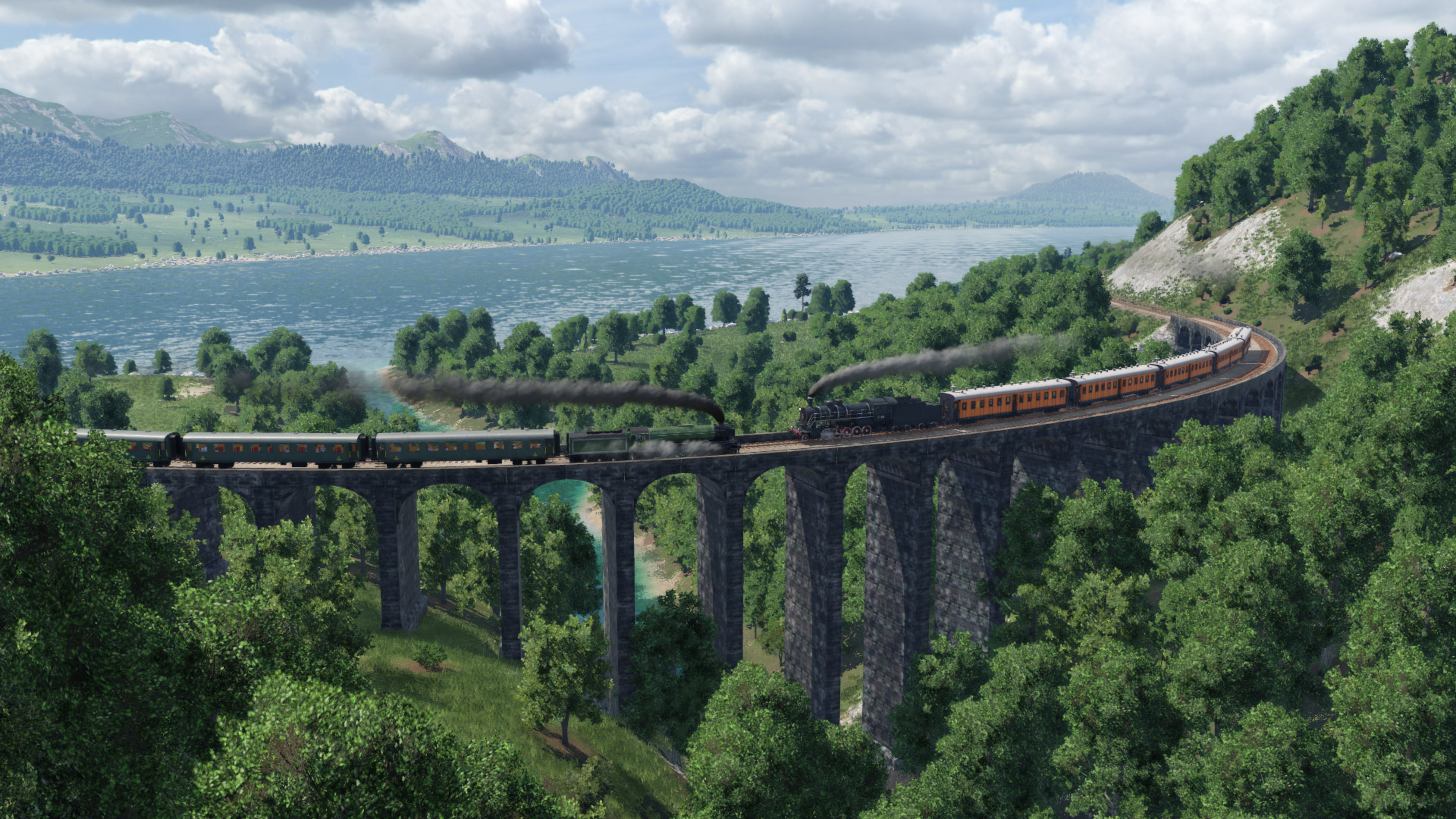 Zug überquert eine Steinbrücke über einem Fluss, umgeben von Bäumen und Bergen im Hintergrund.