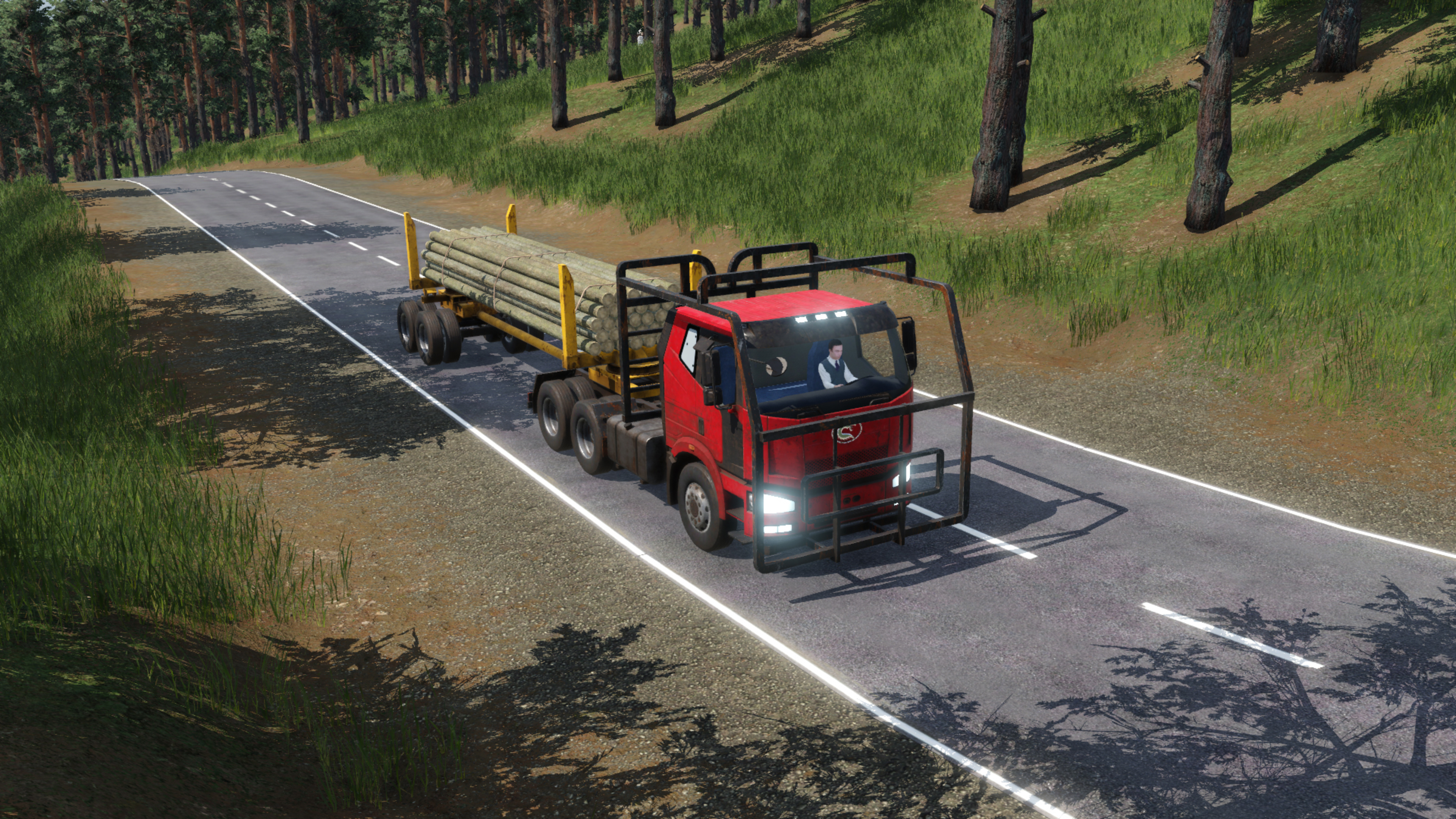 Roter Holztransporter auf einer Straße, transportiert Holzstämme. Grüne Felder und Bäume säumen die Straße. Sonniger Tag, klarer Himmel.