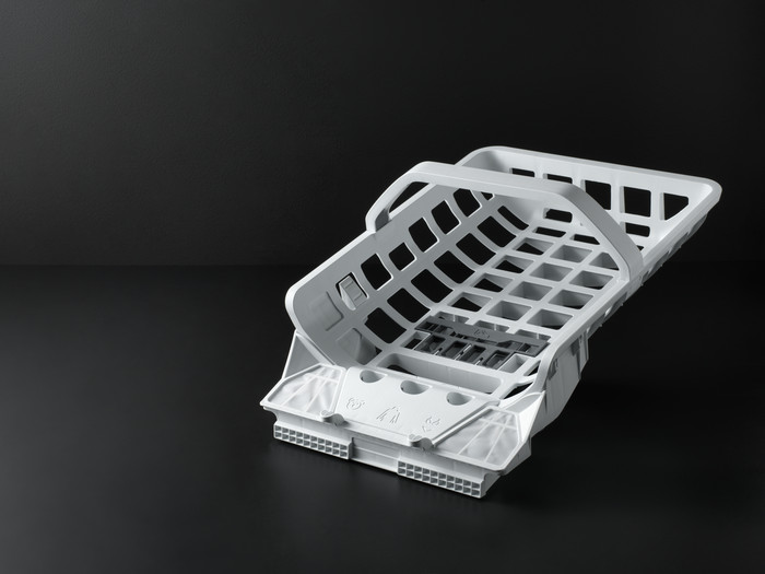 Un panier de lave-vaisselle blanc posé sur une surface noire, le panier est ouvert.