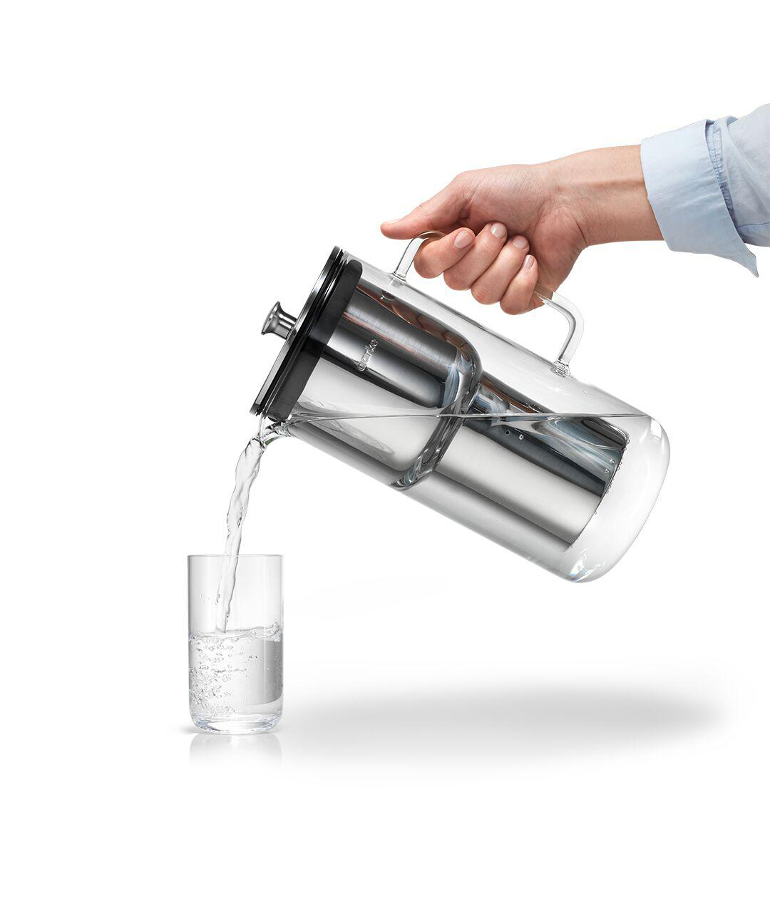 Hand gießt Wasser aus einem durchsichtigen Krug in ein Glas, weißer Hintergrund.
