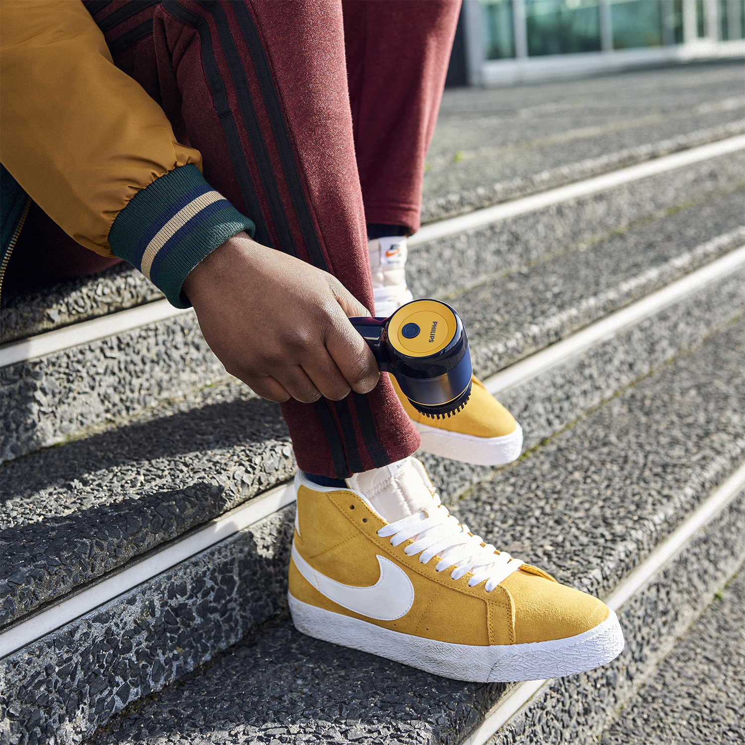 Persona con scarpe da ginnastica gialle con logo Nike bianco e nero, che le pulisce con un dispositivo portatile.