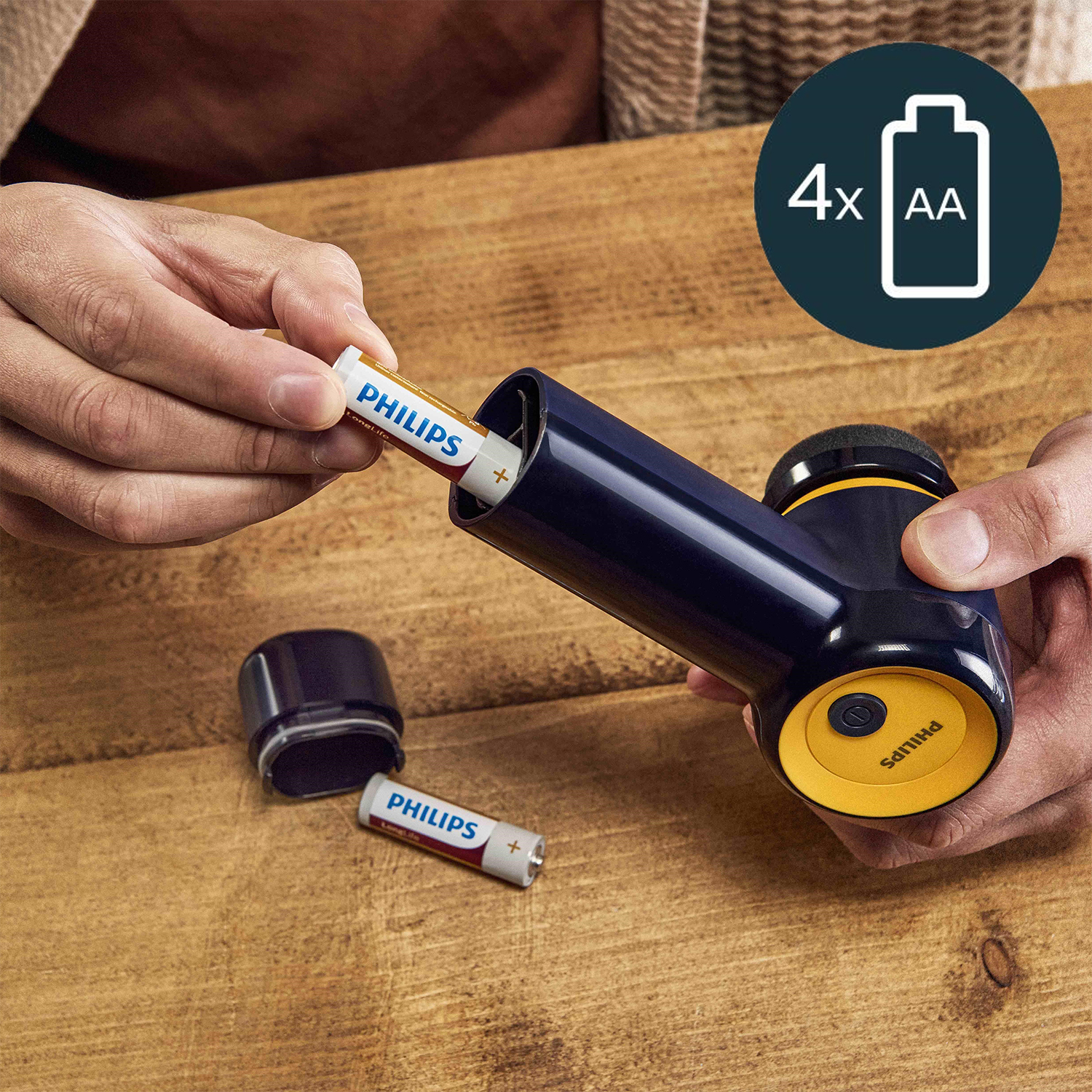 Una persona inserisce una batteria Philips in un dispositivo blu scuro e giallo, un'altra batteria è visibile.