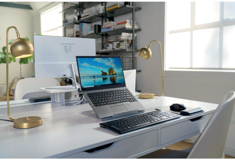 Munkahely laptop, monitor, billentyűzet, egér és két arany asztali lámpával. Fehér asztal.
