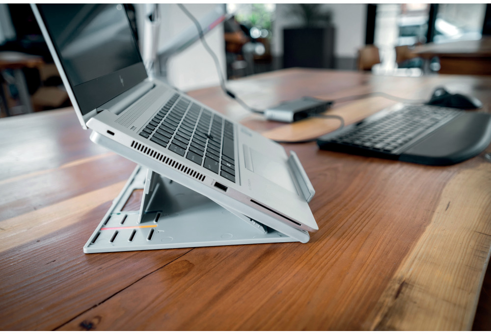 Laptop egy állványon egy fa asztalon. Egy billentyűzet van az oldalon.