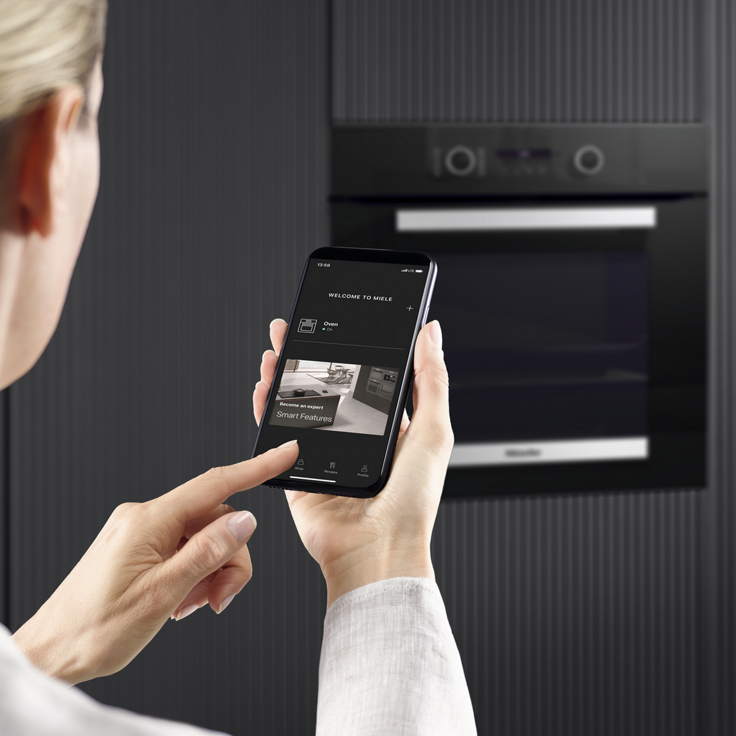 Woman using a phone, showing smart features from oven, in front of a black oven.