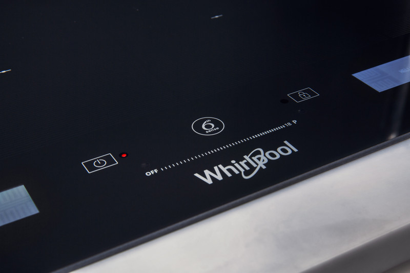 Közelkép egy Whirlpool főzőlapról, bekapcsolás- és zárjelzőkkel. Fekete és fényes.