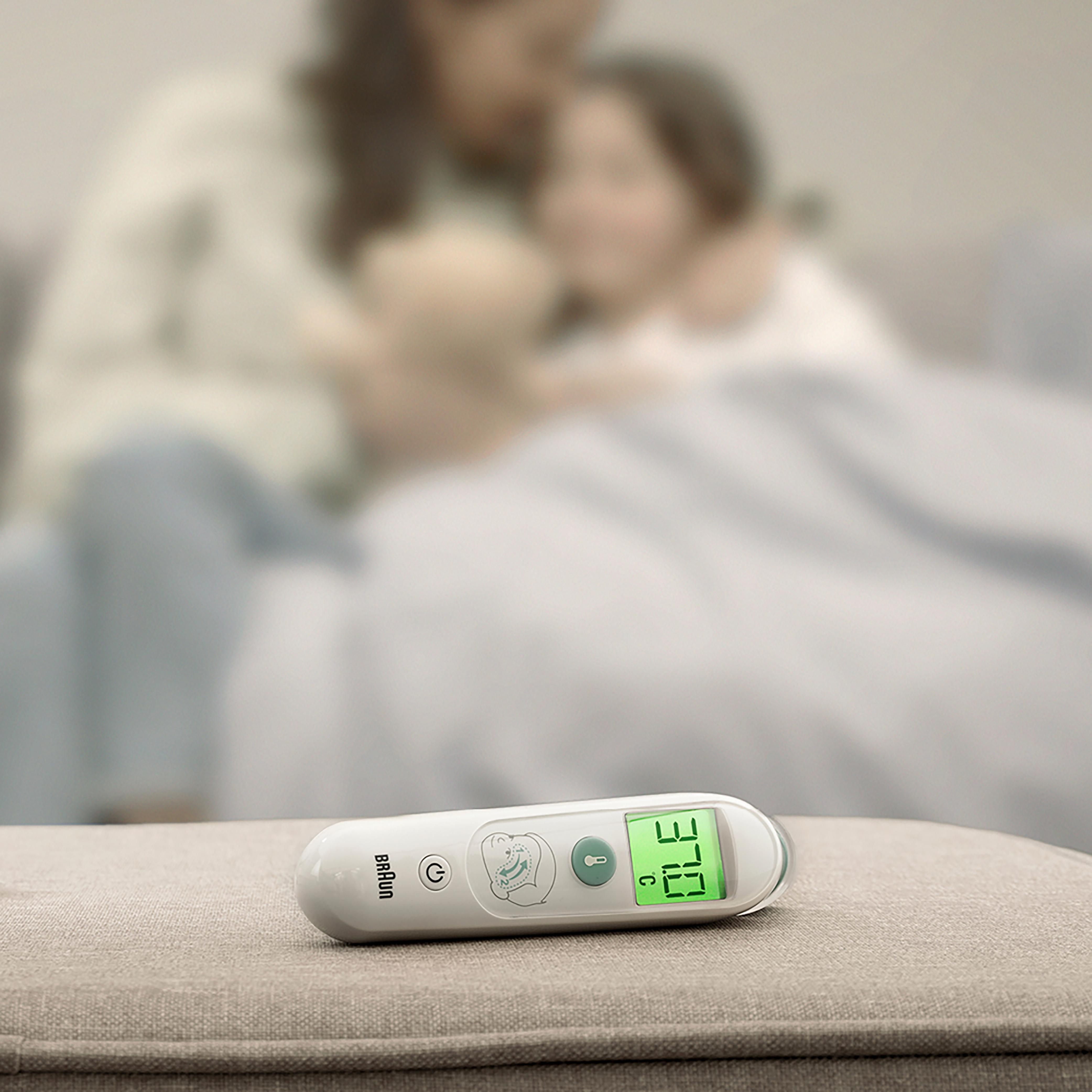 Thermometer mit grüner Anzeige. Verschwommener Hintergrund zeigt Frau und Kind.