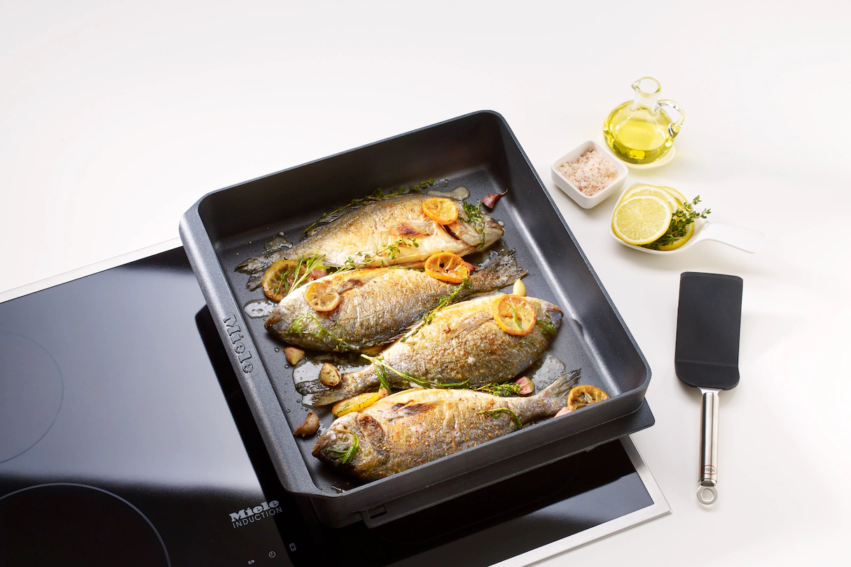 Gebackener Fisch in einer Pfanne mit Zitronenscheiben und Öl. Spatel und Salz.