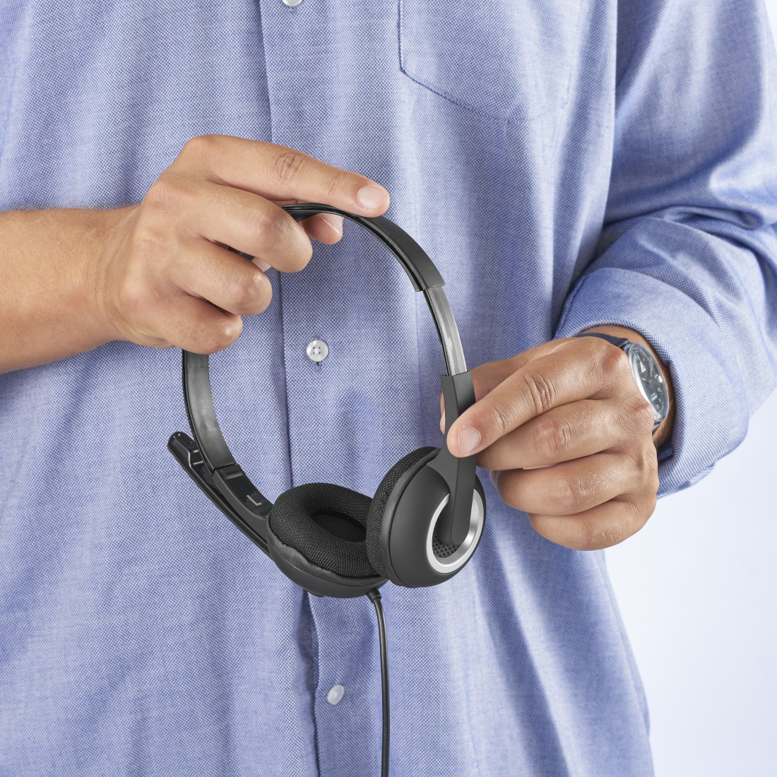 Persona sosteniendo unos auriculares negros con micrófono y camisa azul.