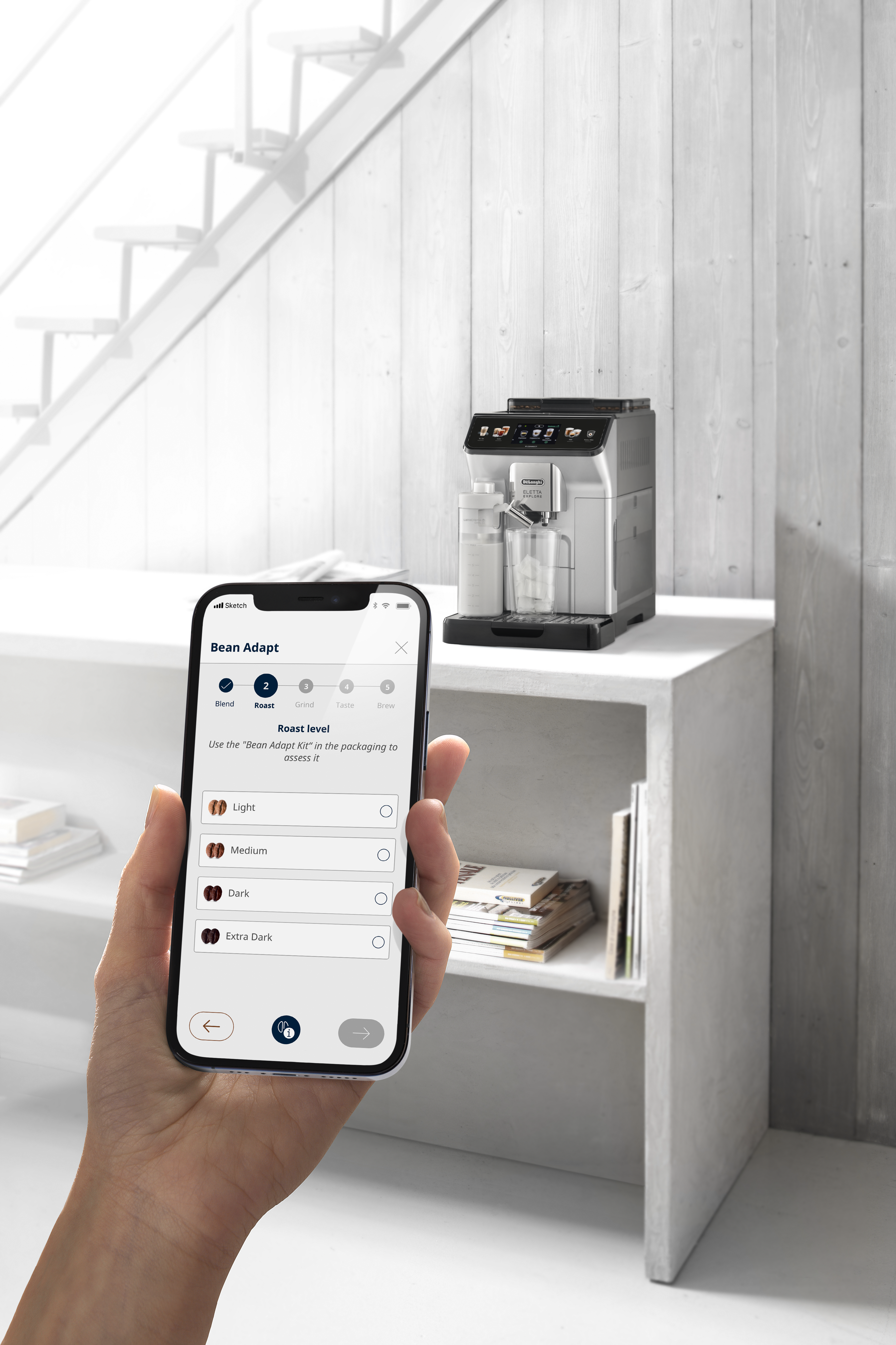 Eine Person hält ein Telefon, Kaffeemaschine im Hintergrund.