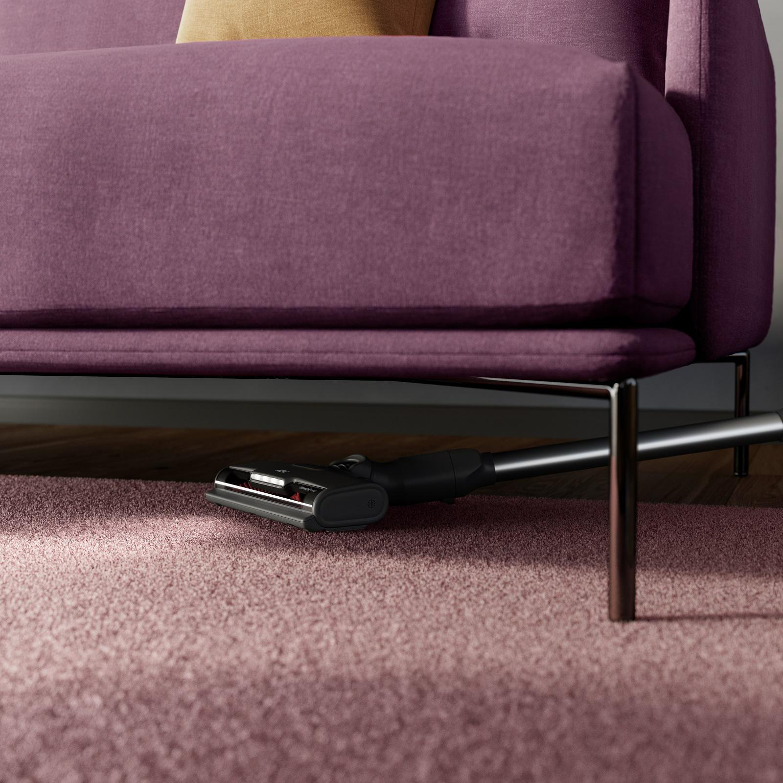 Staubsaugerkopf unter einem lila Sofa, mit einem rosa Teppich.