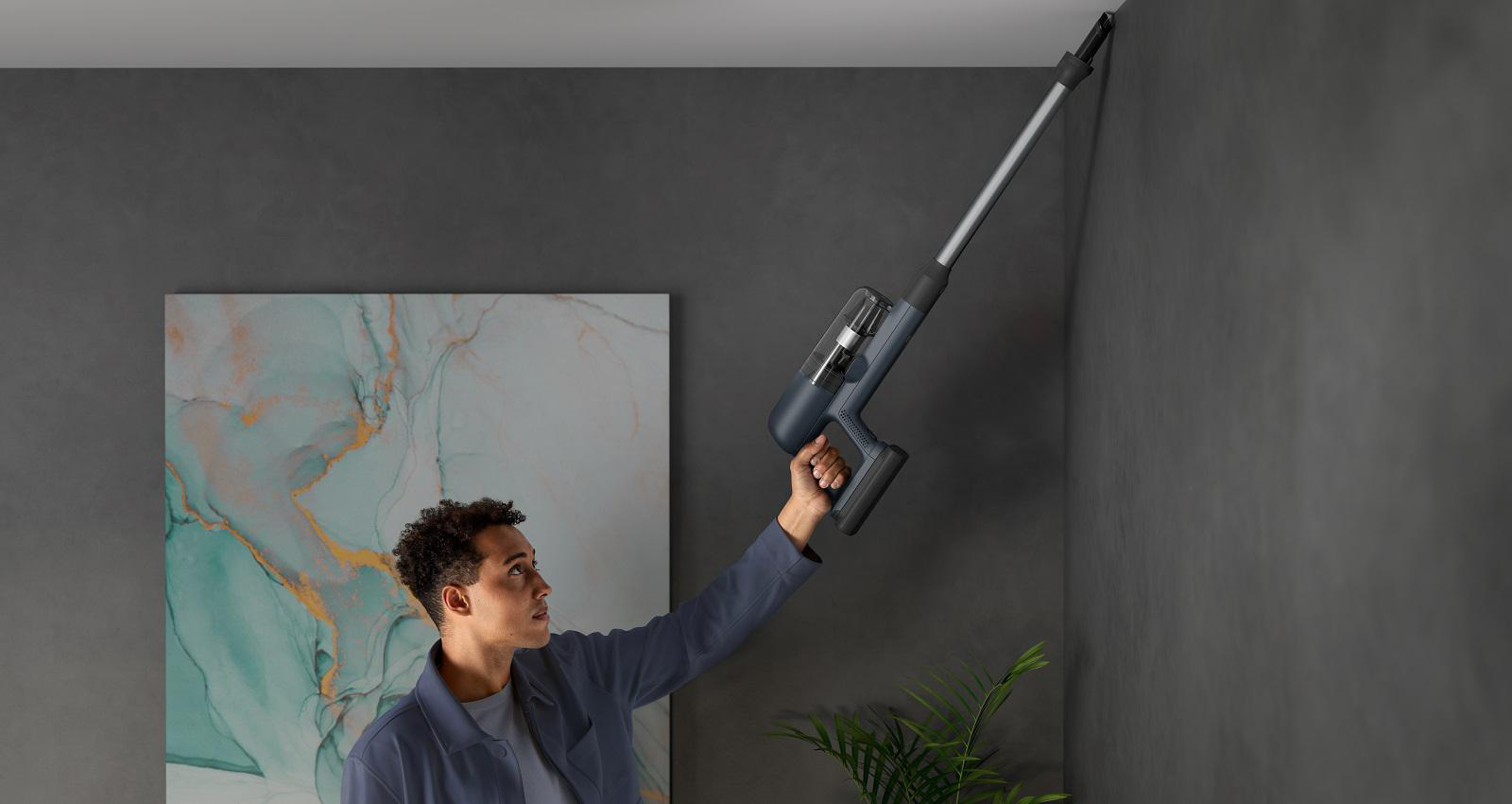 Ein Mann benutzt einen kabellosen Staubsauger an einer grauen Wand.