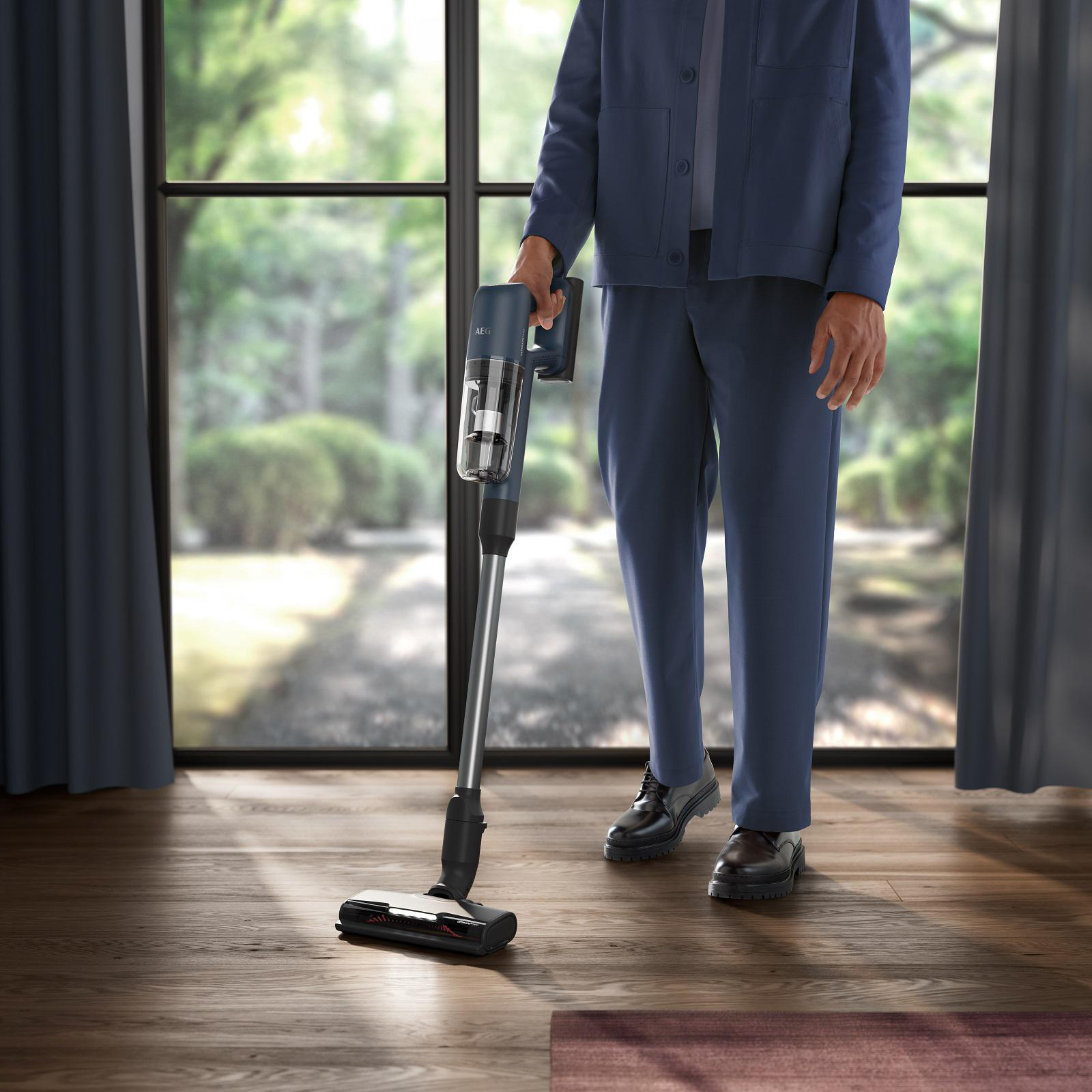 Eine Person in einem blauen Anzug benutzt einen Stielstaubsauger auf einem Holzboden.