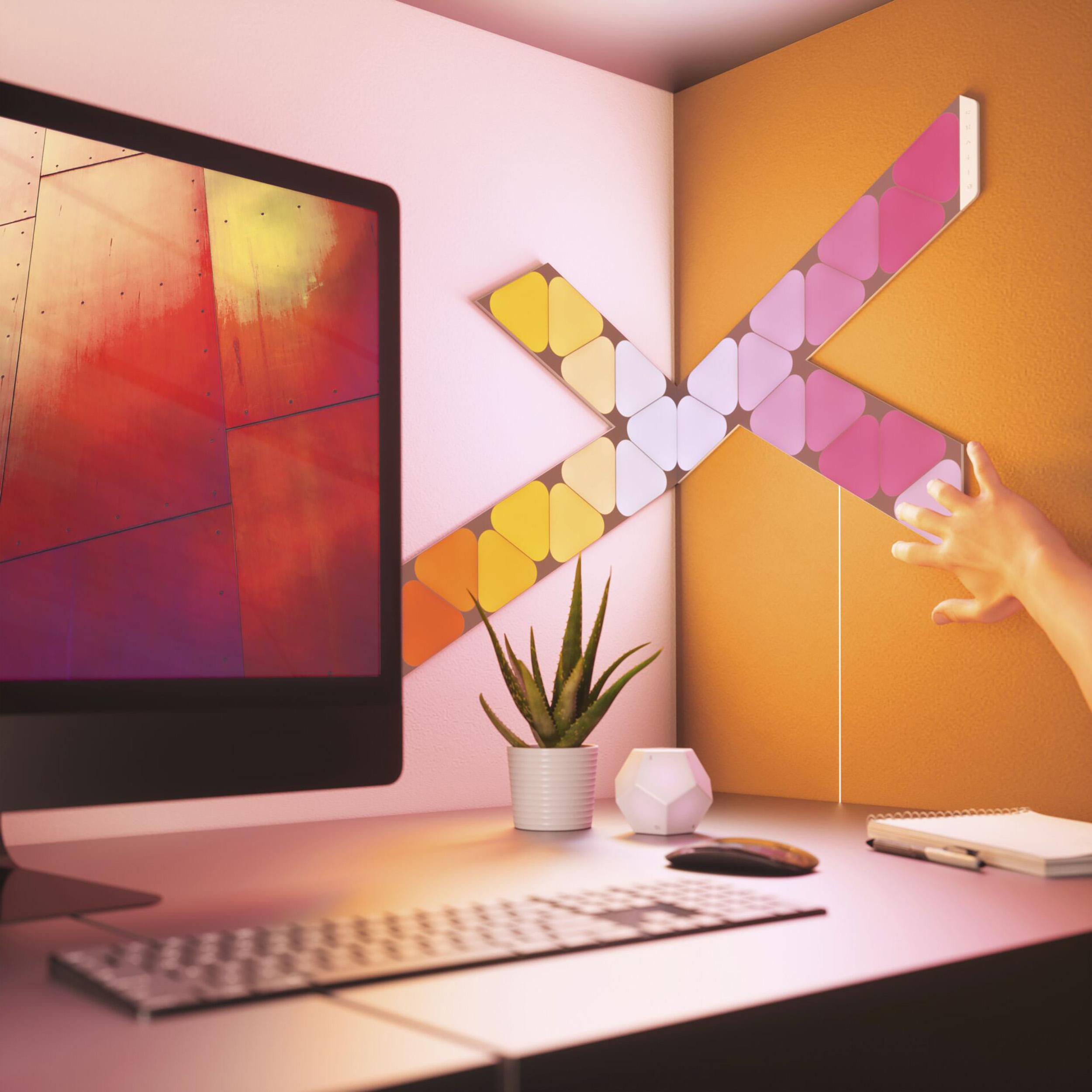 Schreibtisch mit Computer, Pflanze und bunten Lichtpaneelen an der Wand.