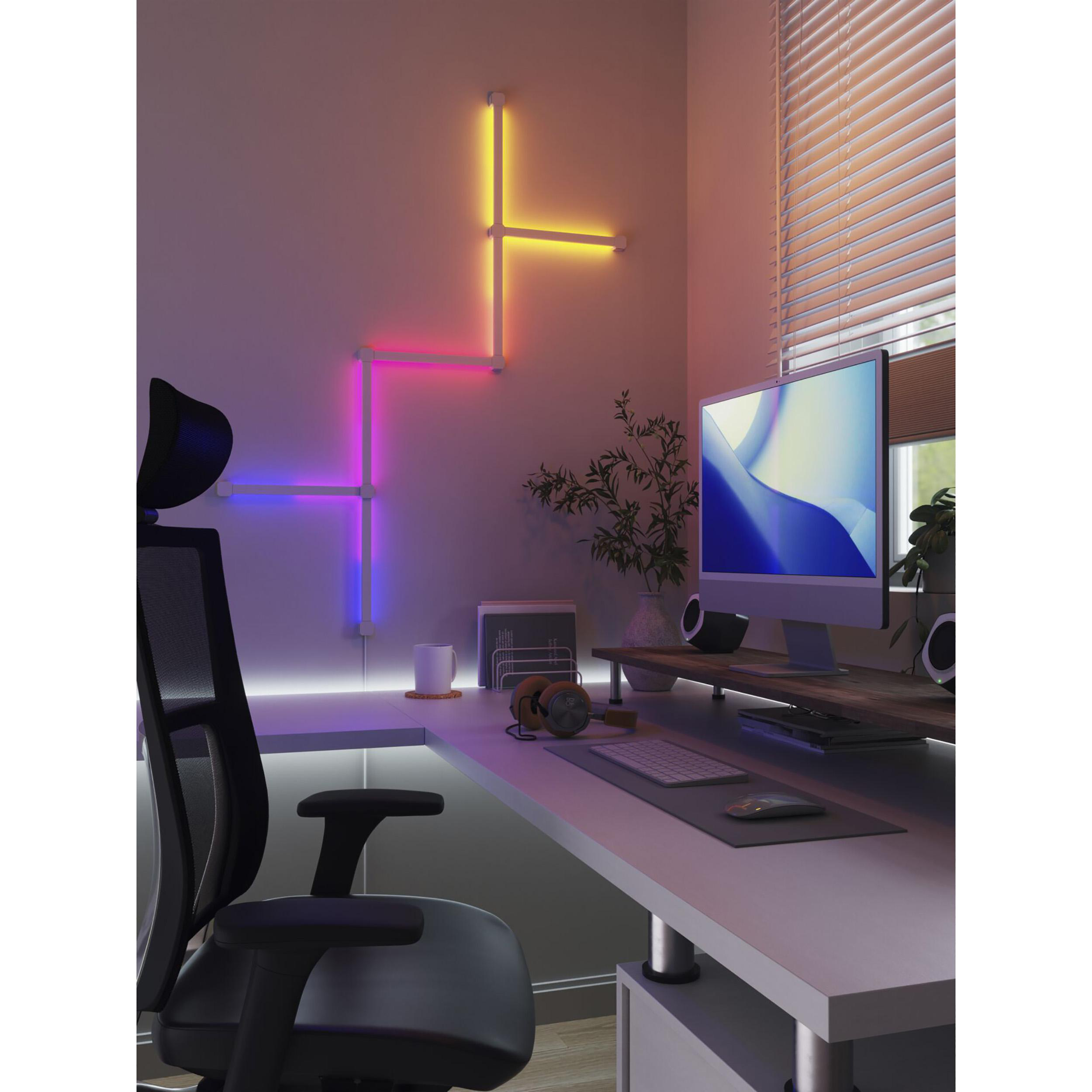 Ein Schreibtisch mit Computer, Kopfhörern und bunten Neonlichtern an der Wand.