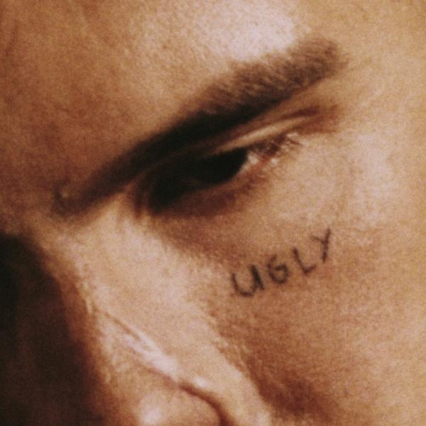 Close-up van een gezicht met het woord 'UGLY' onder het oog getatoeëerd.