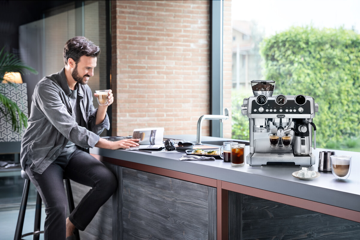 Uomo seduto a un bancone della cucina, usa un laptop, vicino a una macchina da caffè e tazze.
