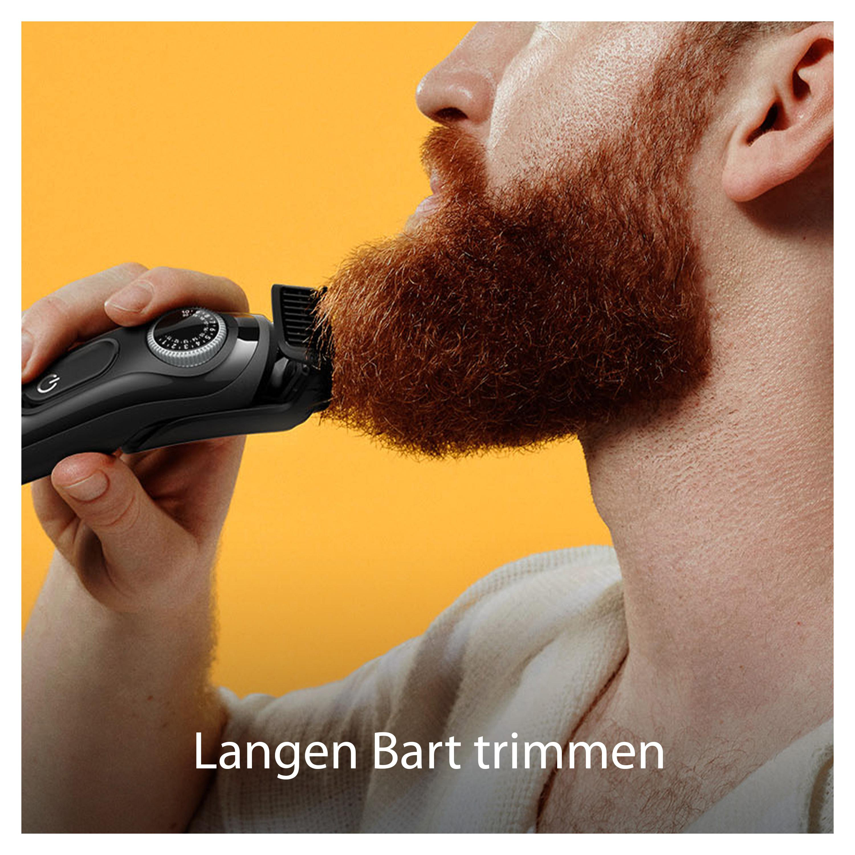 Ein Mann trimmt seinen langen Bart mit einem elektrischen Bartschneider.