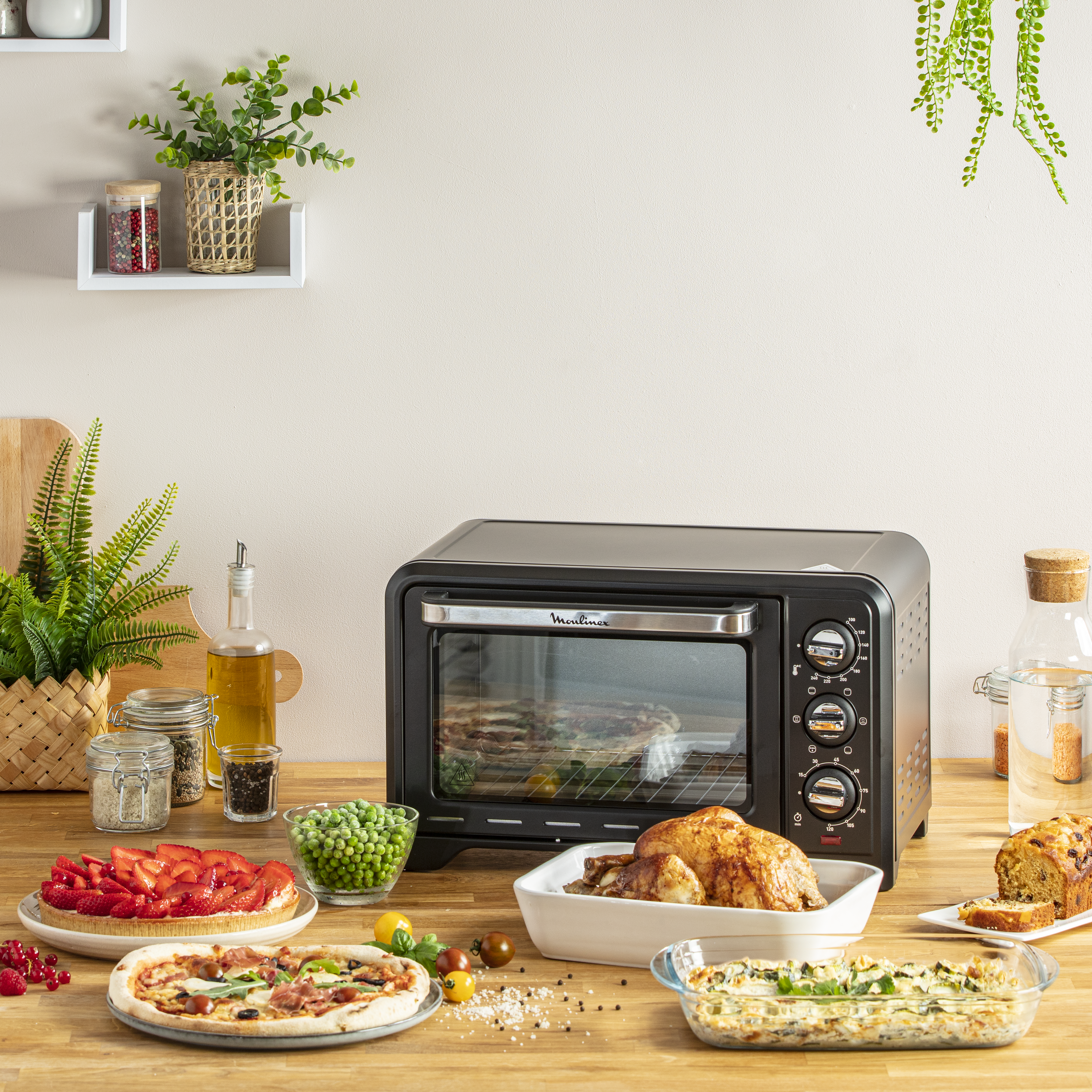 Escena de cocina con horno, comida e ingredientes en una mesa de madera. Incluye pollo asado, pizza y tarta de fresas.