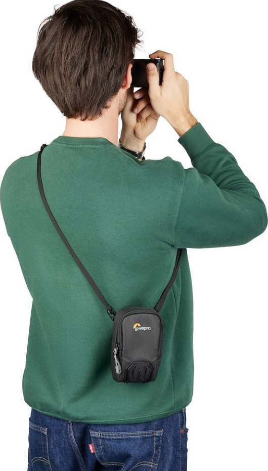 Uomo che scatta una foto con la fotocamera in alto, indossa una camicia verde e una borsa per fotocamera.