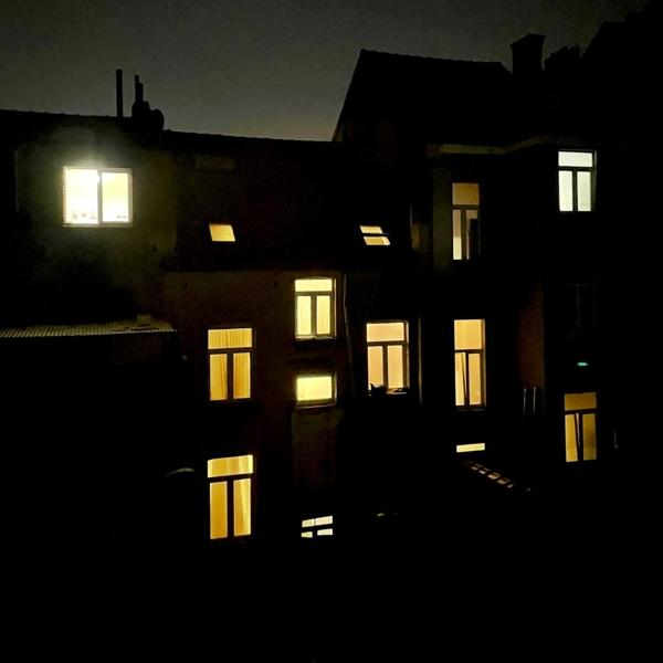 Donkere nachtscène van een gebouw met verlichte ramen. De ramen zijn van verschillende maten en vormen, die geel licht werpen.