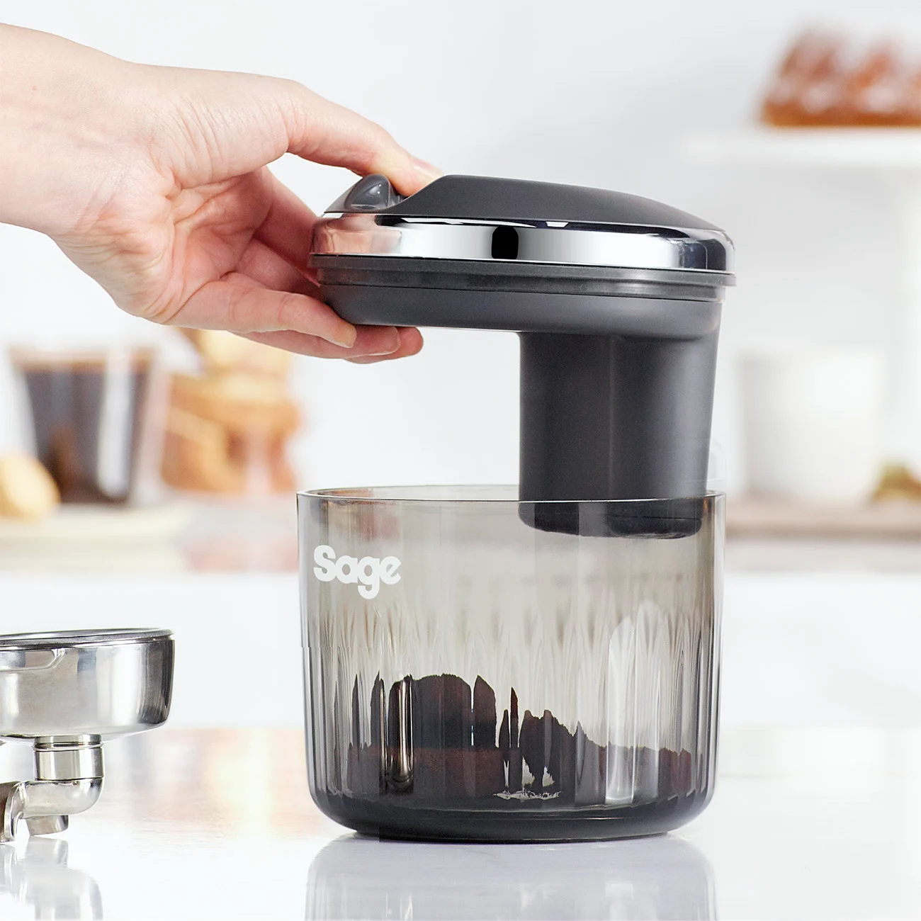 Hand gießt Kaffeepulver in einen transparenten Behälter.