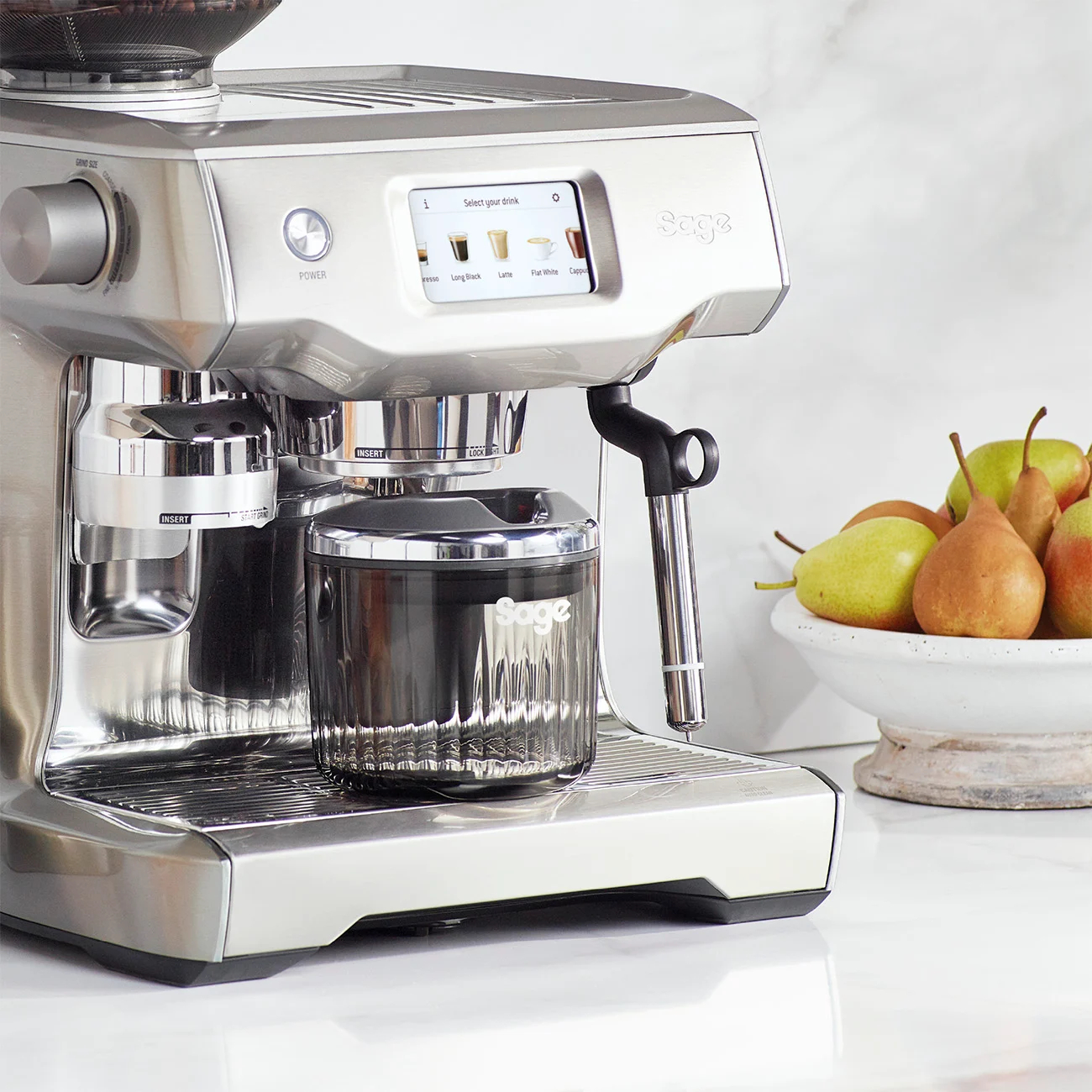Eine silberne Espressomaschine mit Touchscreen, einer Tasse und einer Schüssel Birnen.