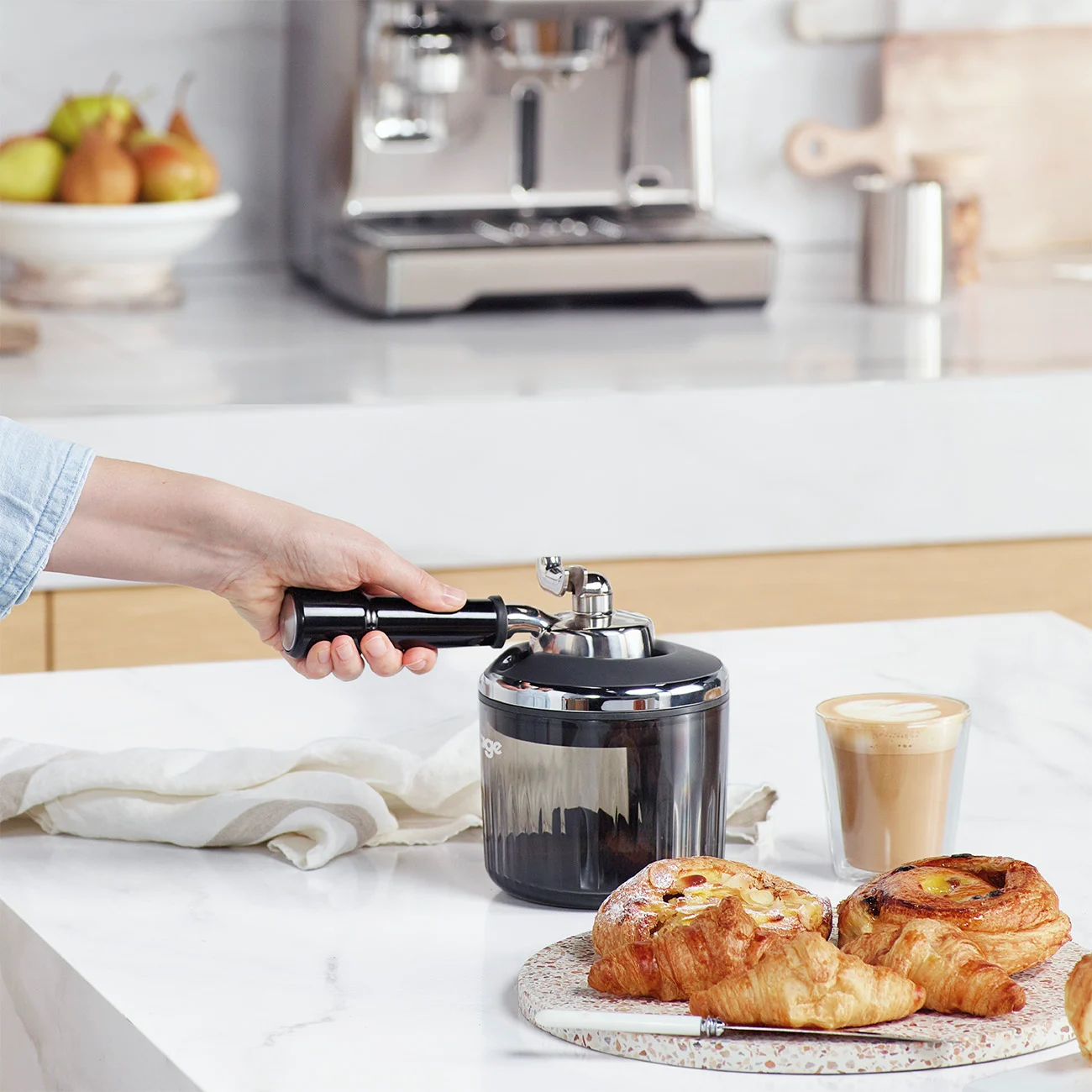 Frau hält den Siebträger einer Kaffeemaschine, Gebäck auf einem Tisch.