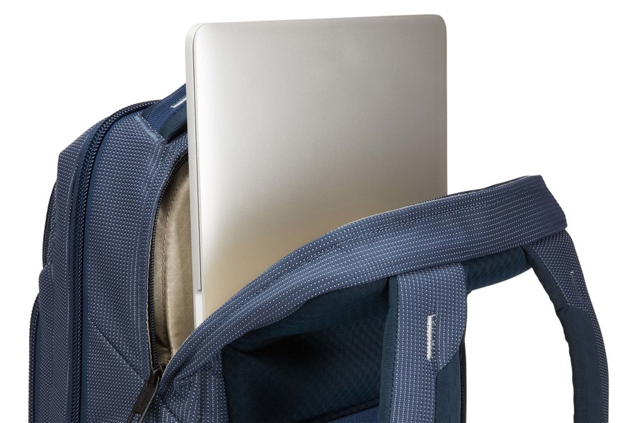 Mochila azul marino con portátil plateado dentro, fondo blanco.