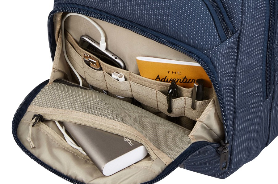 Mochila con compartimentos abiertos: un teléfono, cargador, cuaderno, bolígrafos y un banco de energía.