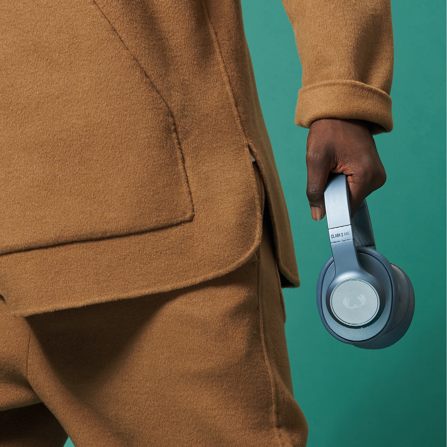 Person in a brown suit holding blue headphones against a teal background.