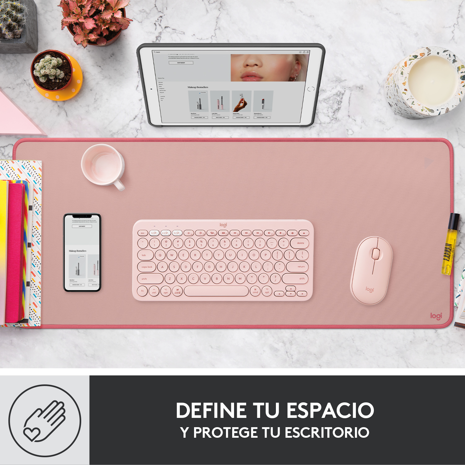 Configuración de escritorio rosa con teclado, ratón, tableta, libros y plantas.