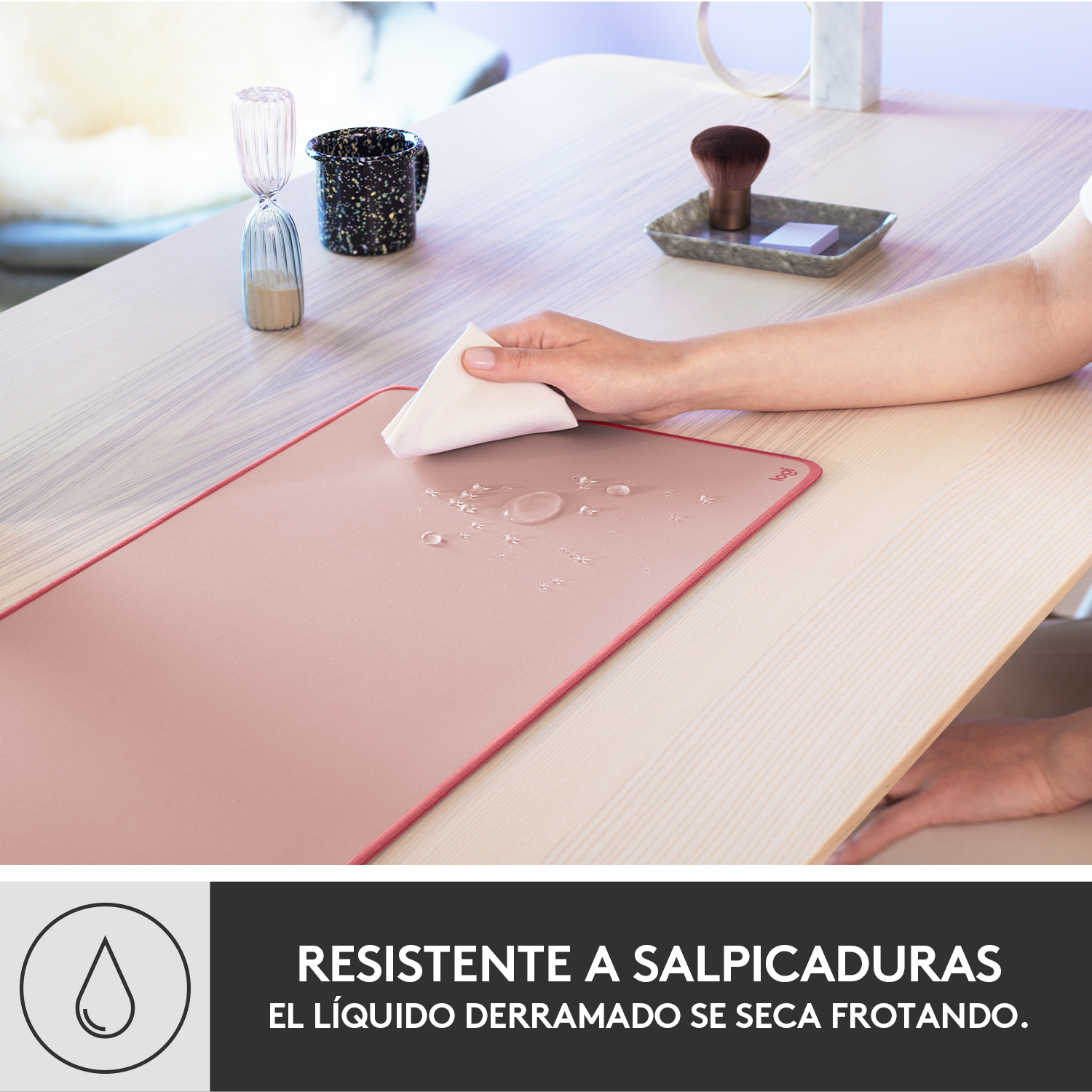 Una alfombrilla de ratón rosa sobre un escritorio de madera con gotas de agua y texto sobre resistencia a derrames.