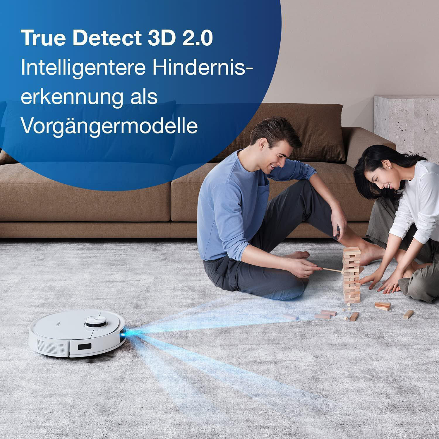 Ein Roboter-Staubsauger reinigt einen Teppich, während Menschen im Hintergrund spielen.