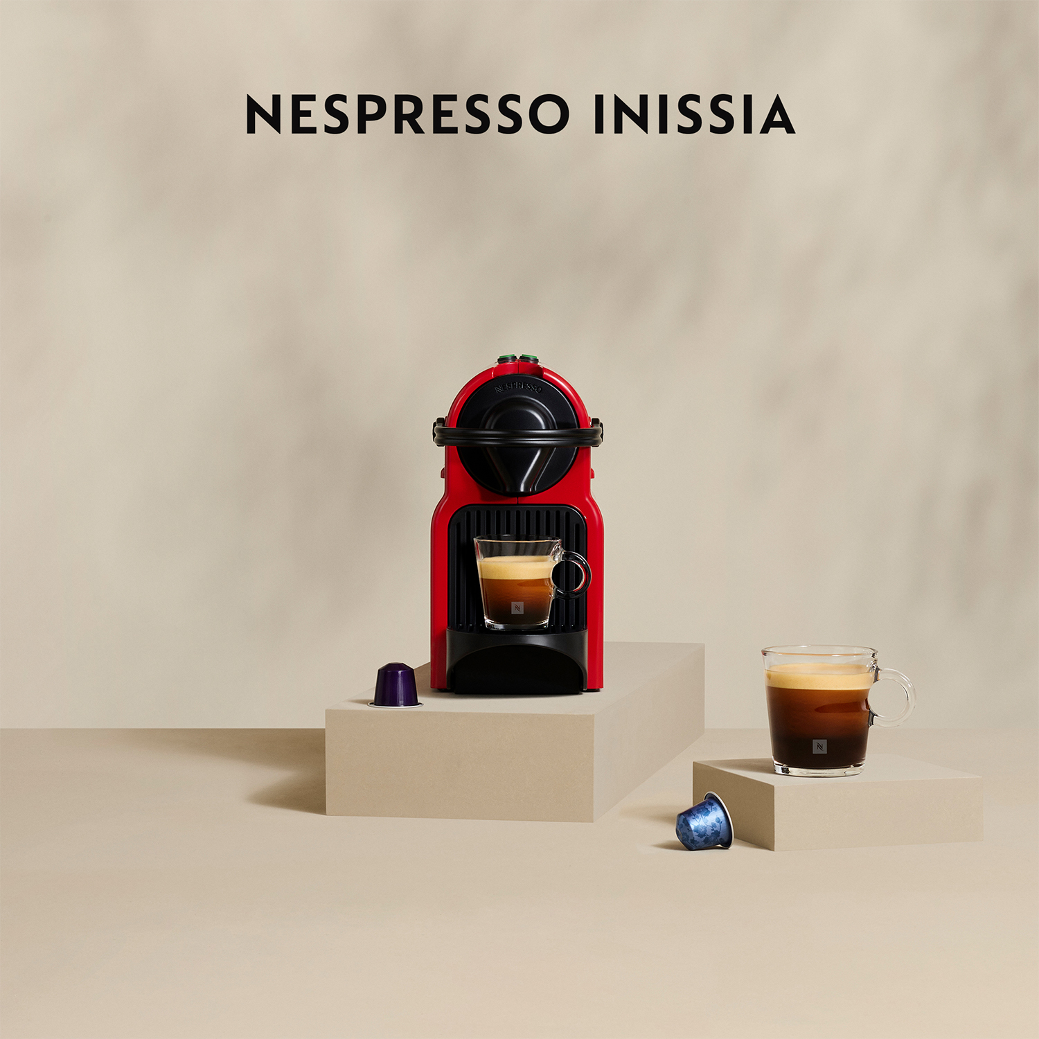 Macchina da caffè Nespresso Inissia rossa con un bicchiere di caffè.