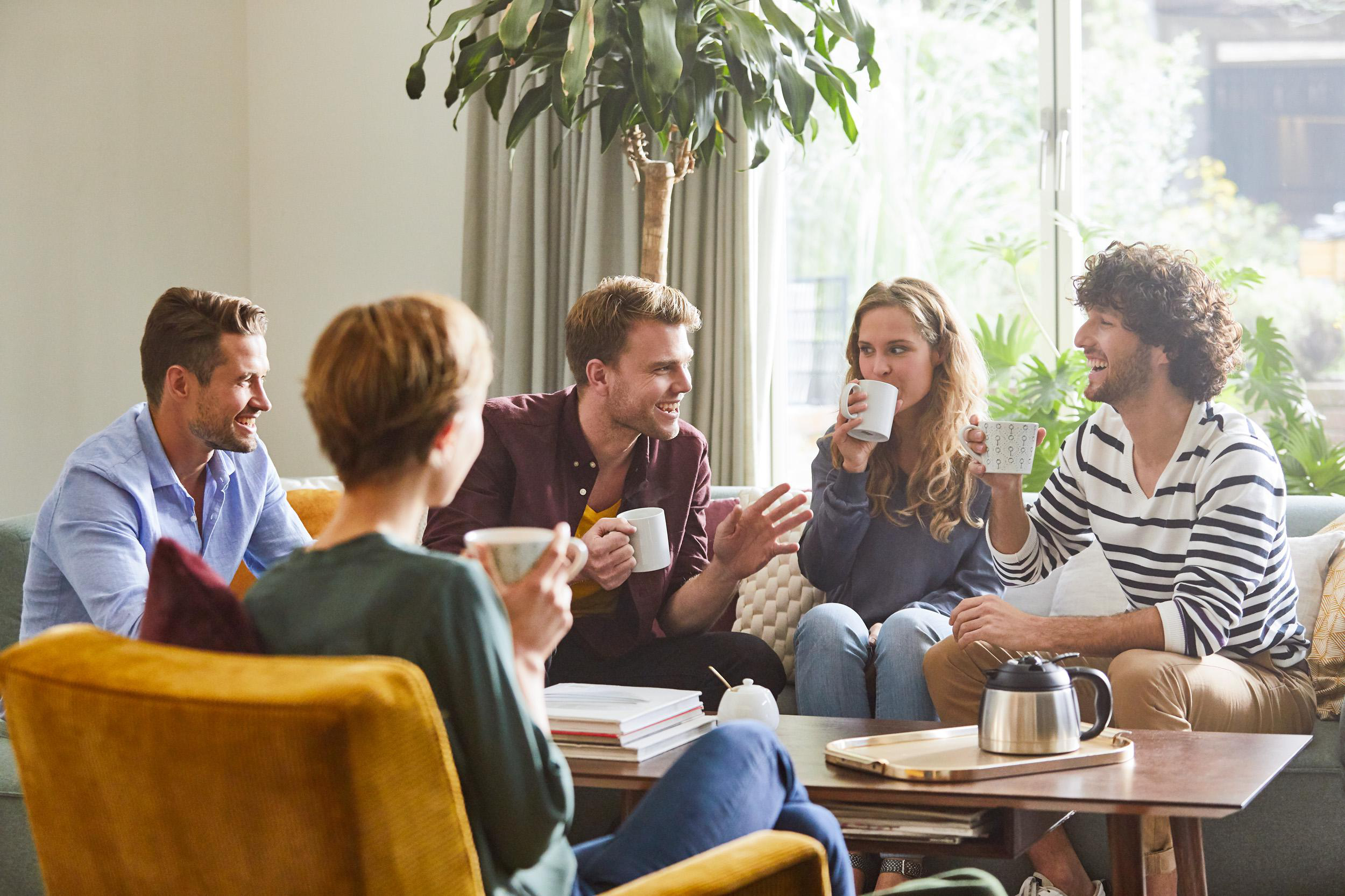 Gruppe von Leuten in einem Wohnzimmer, die Kaffee trinken und reden.